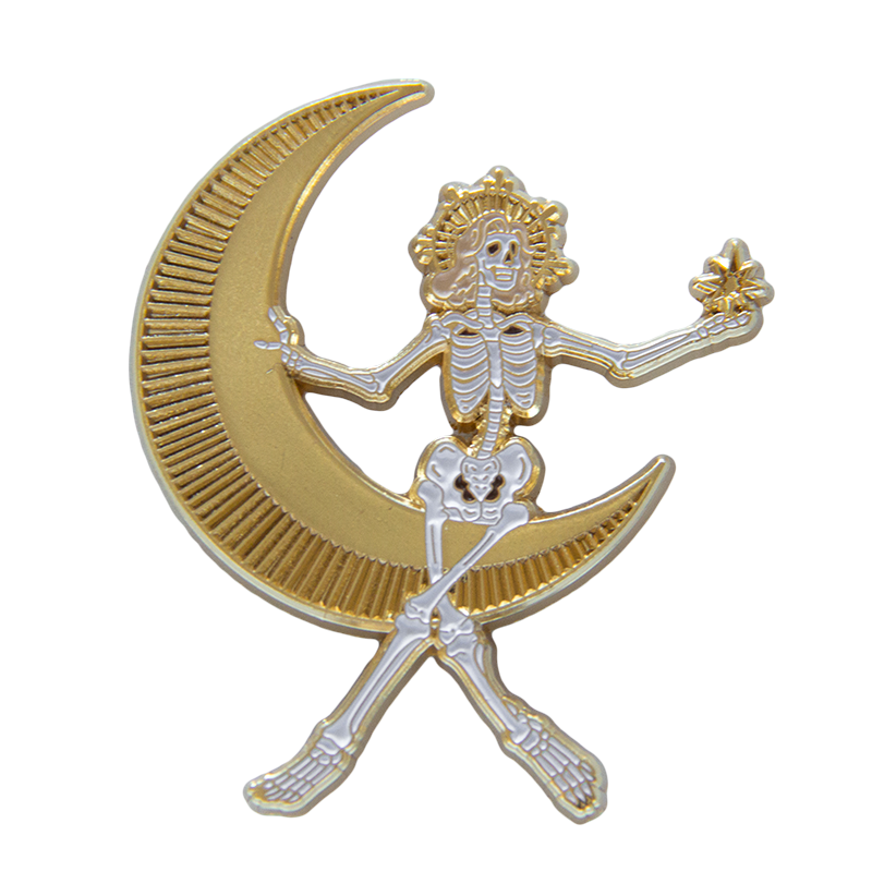 A gold and white enamel pin of a skeleton woman sitting in the moon for dark elegant fashion. 