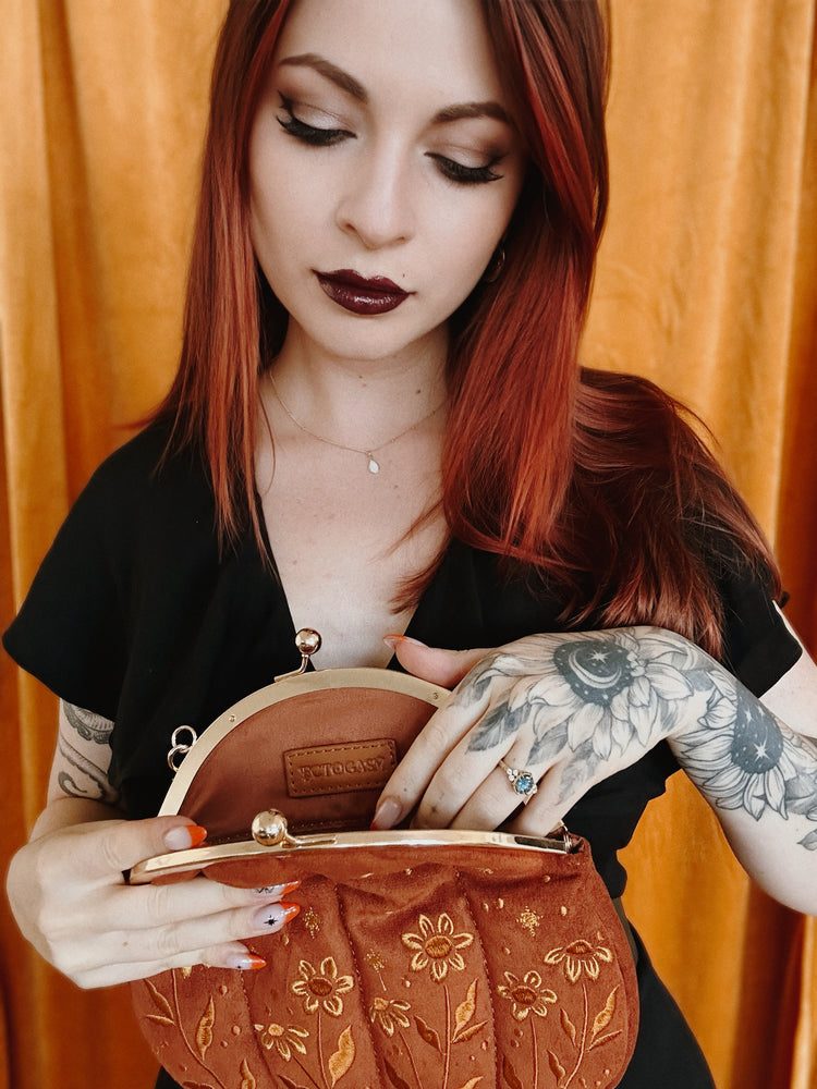 A woman opening a vintage inspired kiss lock purse shaped like a pumpkin for fall fashion in orange, yellow, and brown. 