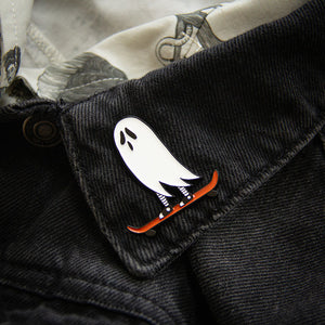 A funny lapel pin for men and women of a spooky black and white ghost skateboarding.