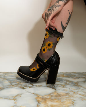 A tattooed woman wearing platform mary jane heels and yellow and black sunflower socks for alternative fashion and summer goth style. 