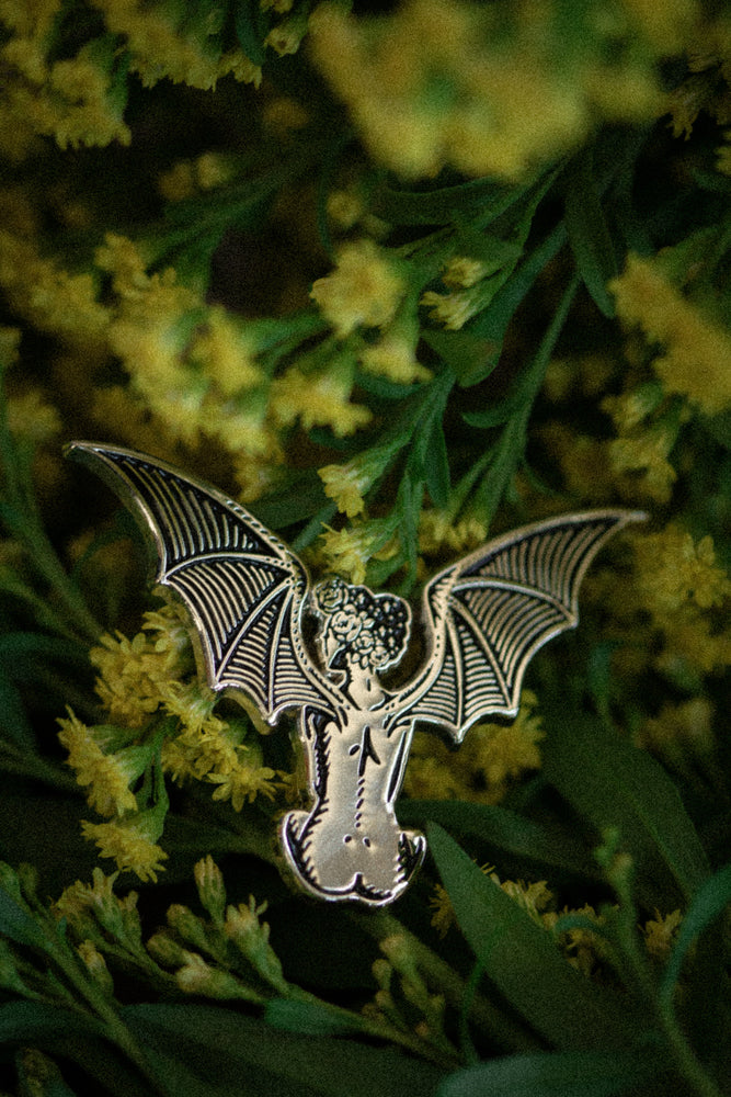 An enamel pin of a vintage style woman with devil's bat wings.