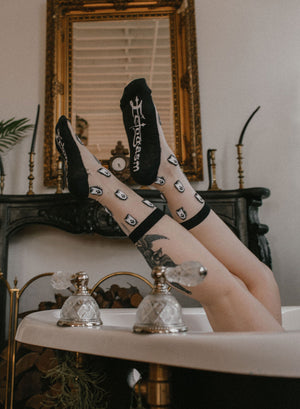 A tattooed woman wearing black and white Ectogasm socks printed with cute ghosts. 