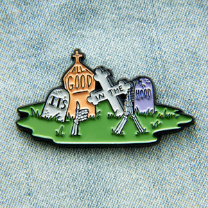 A dark humor enamel pin of a graveyard with the quote, "It's All Good in the Hood". 