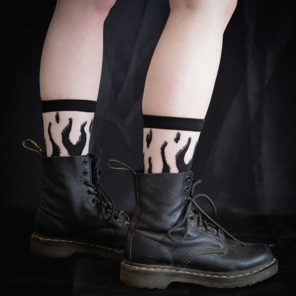 Devil inspired fashion socks that feature a black flame print. Shown worn with a pair of black Doc Marten combat boots for punk style. 