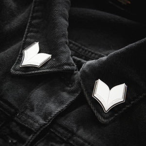 A set of enamel collar pins shaped like open books in black, silver, and white. 