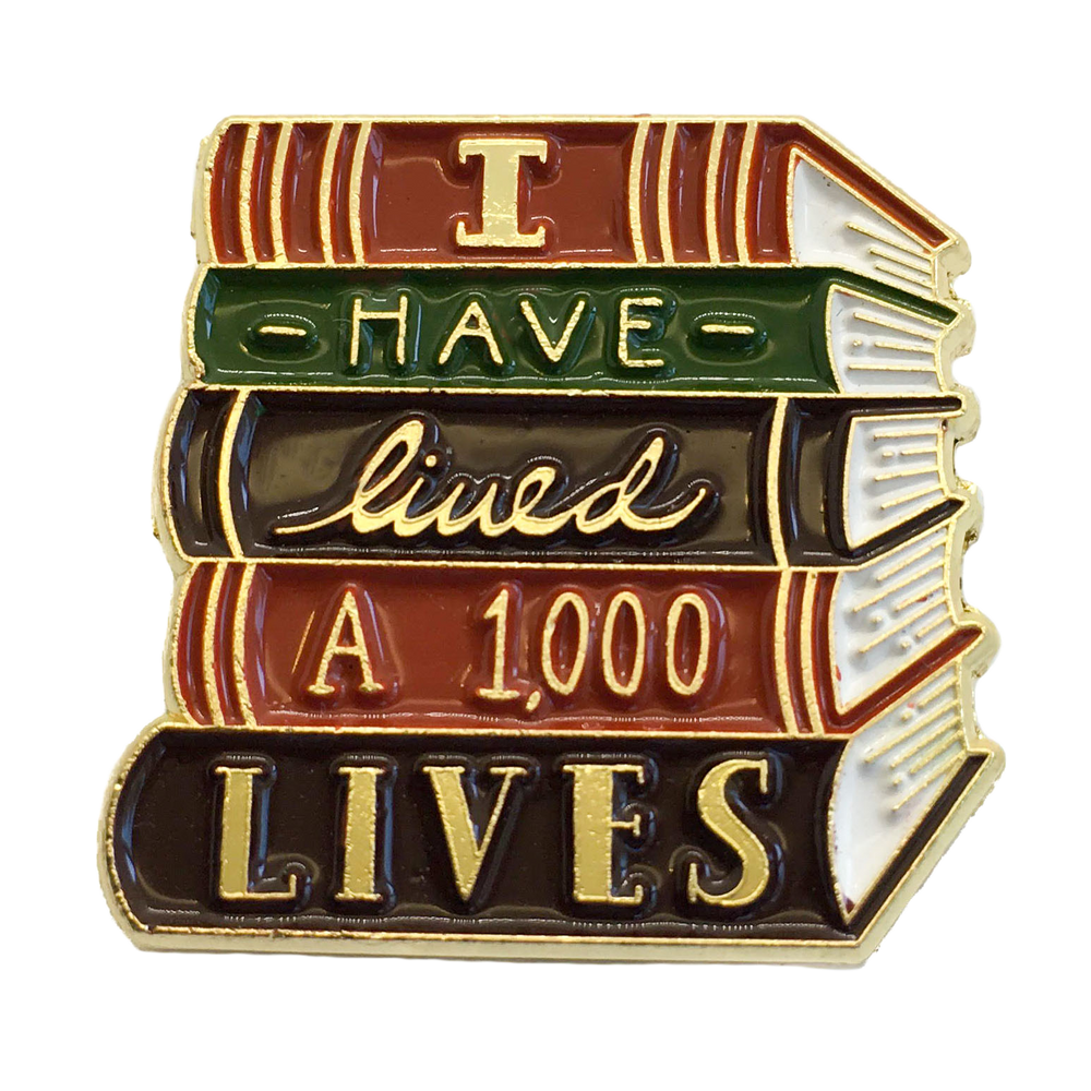 An enamel pin of a stack of books with the quote, "I have lived one thousand lives. 