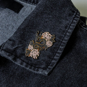 A beautiful lapel pin of a snake with florals on a denim jacket. 
