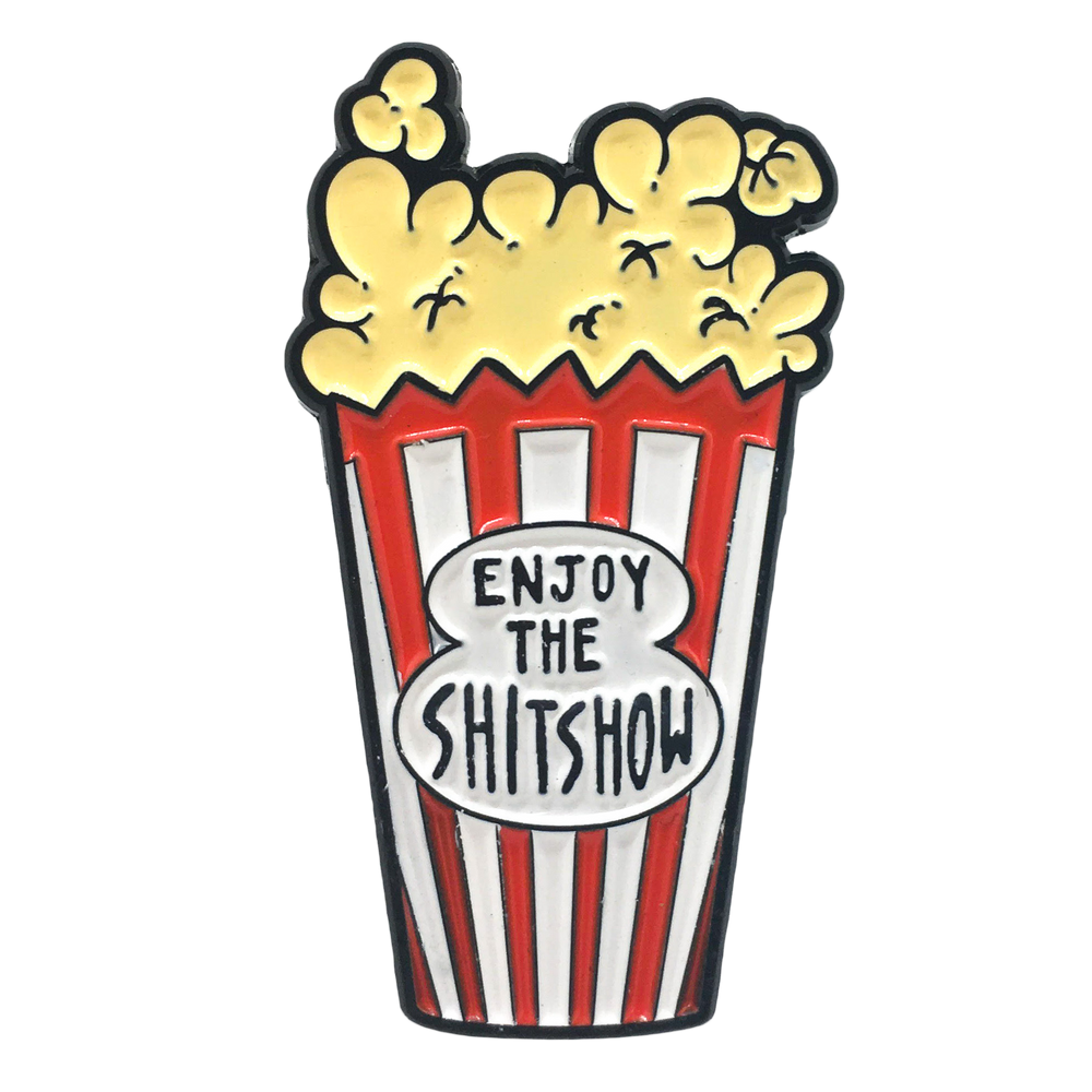 A funny enamel pin of movie theater popcorn with the quote, "enjoy the shitshow" on it. 