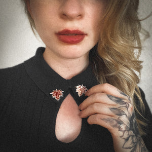 A woman with red lipstick wearing matching red fall leaf jewelry collar pins for dark academia fashion.  
