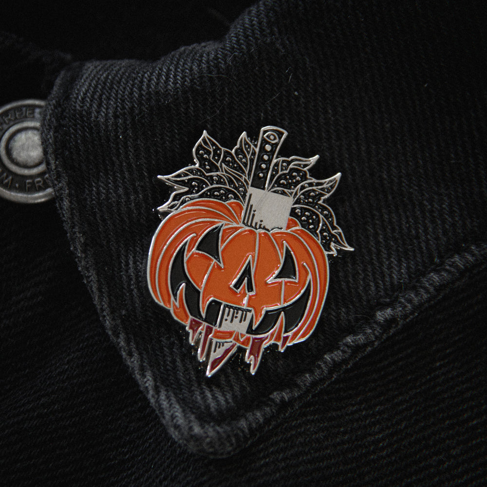 A spooky horror themed lapel pin of a carved pumpkin that's been skewered on a knife.  Great for dark fashion and halloween style. 