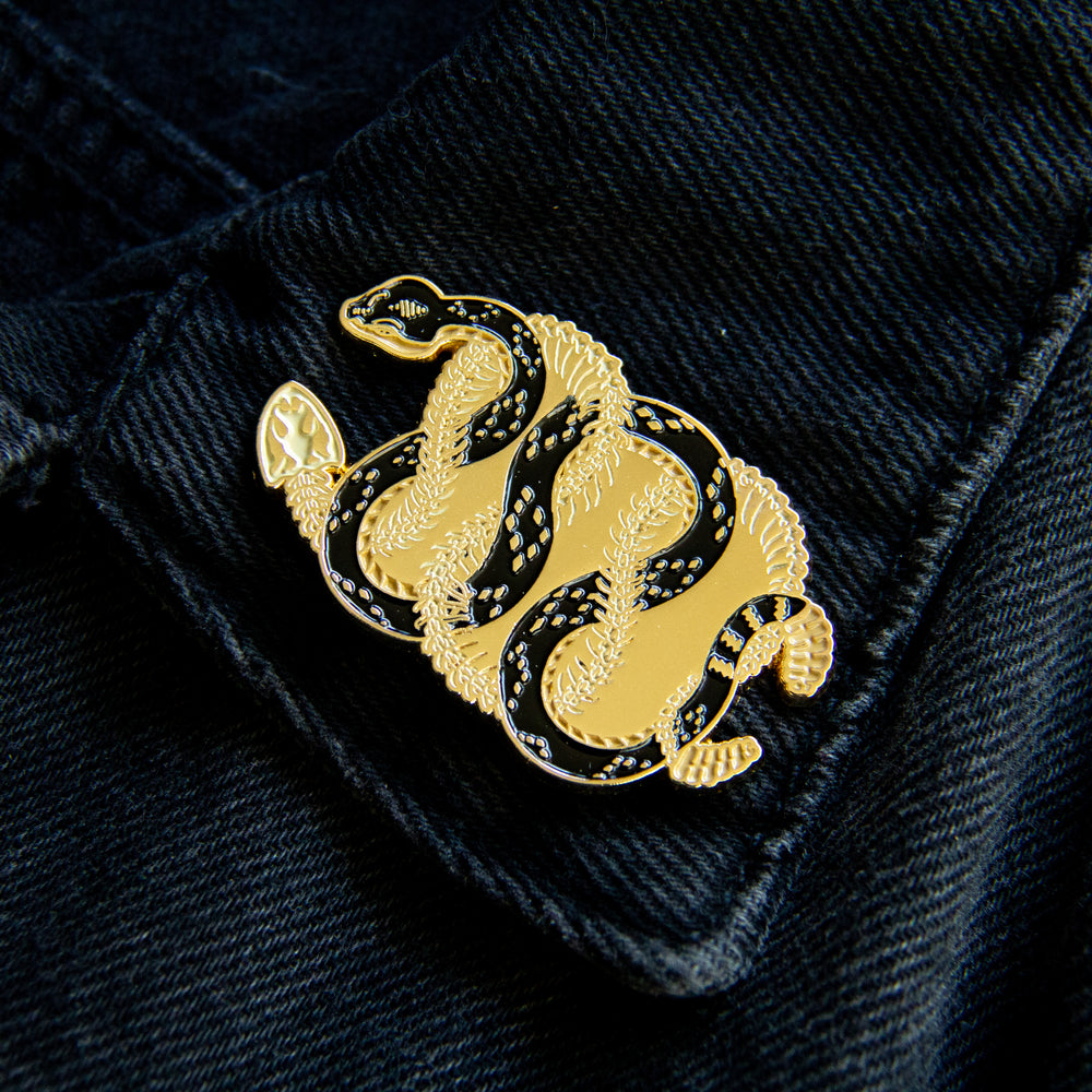 A cool black and gold enamel pin of two rattlesnakes entwined for boho dessert fashion. 
