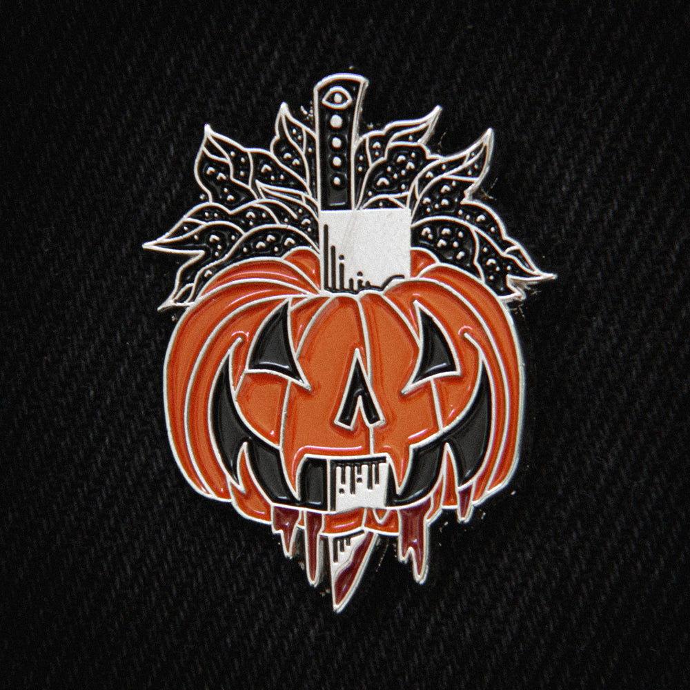A scary enamel pin of a jack-o-lantern pumpkin that's been stabbed with a big kitchen knife and is oozing blood. Great for alternative fashion. 