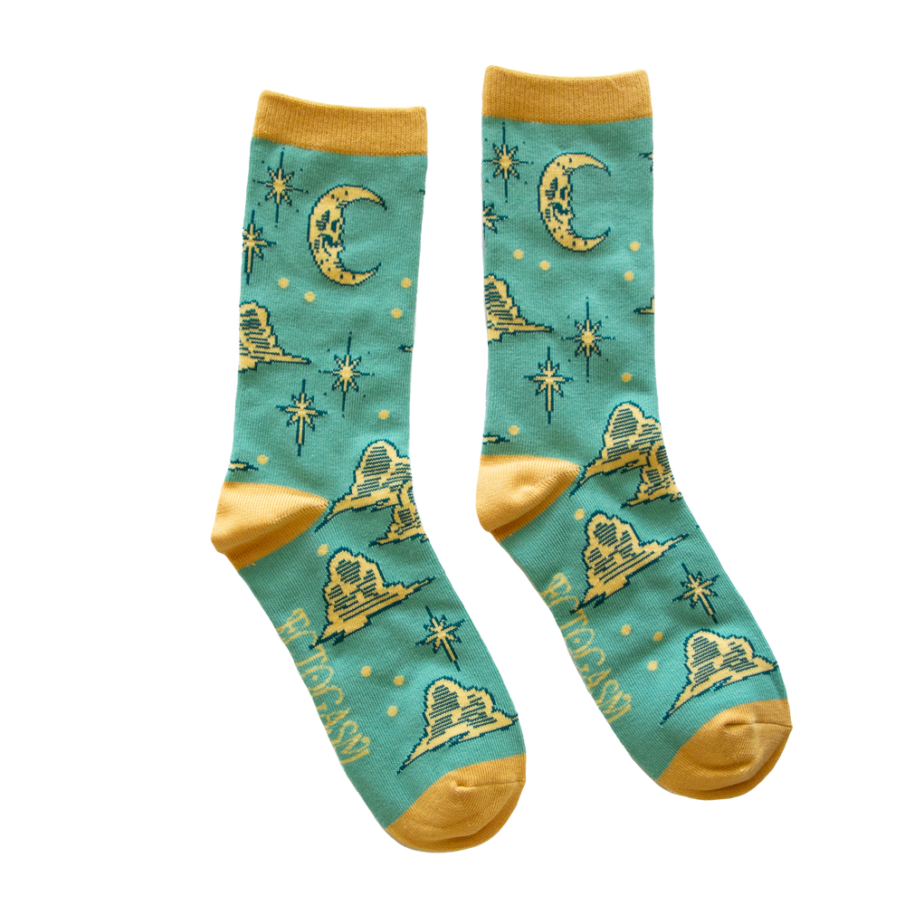 Ectogasm unisex crew socks in teal and gold. Pattern features stars, clouds, and a skull shaped moon, drawn in a vintage style. 