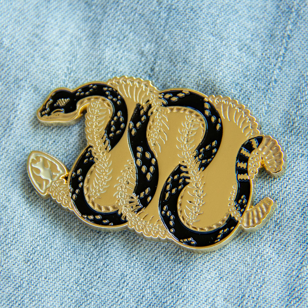 A highly detailed black and gold enamel pin of two snakes for cool witchy style. 