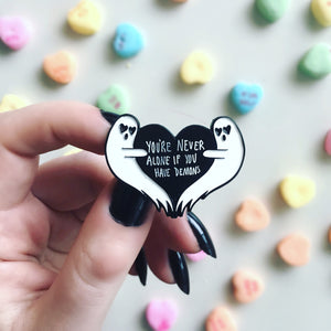 A funny, dark humor enamel pin of ghosts with a black heart. 