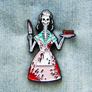 A horror enamel pin of a skeleton dressed as a vintage diner waitress, covered in blood. She has a cherry pie in one hand and a knife in the other.
