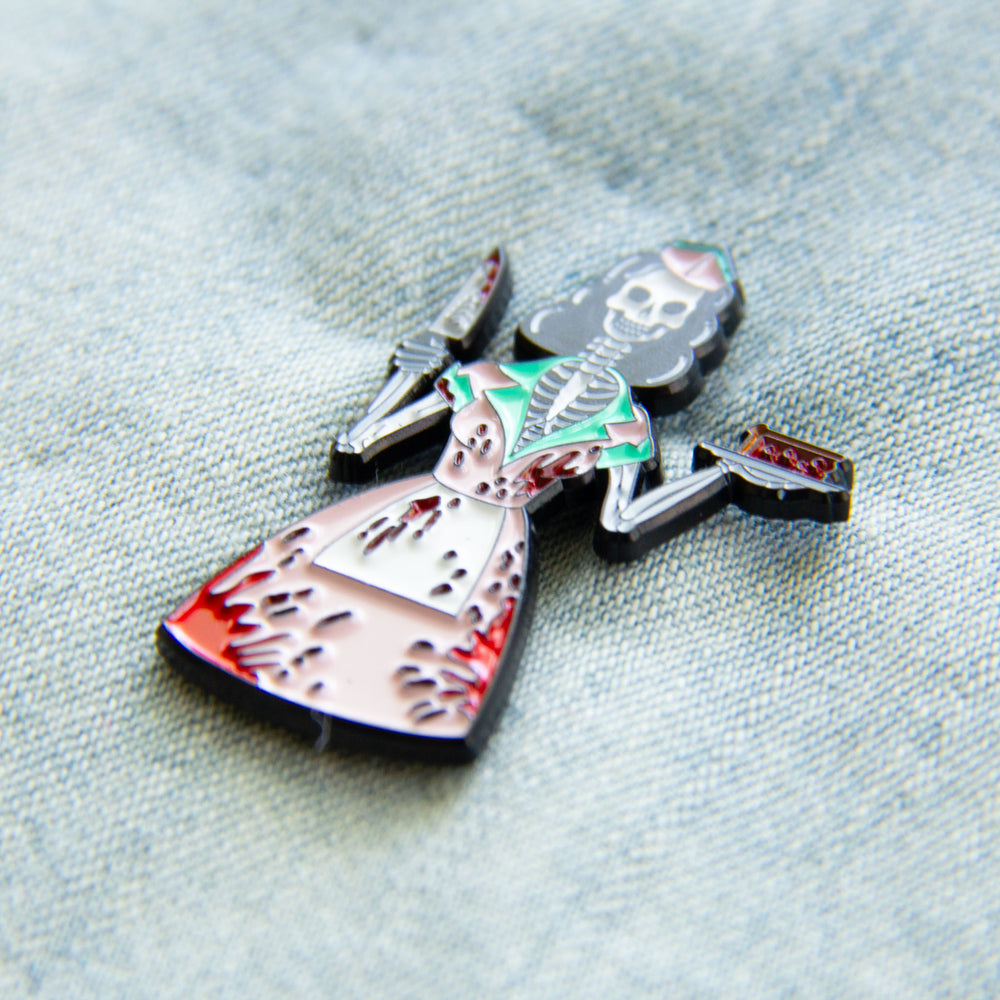 A rockabilly fashion lapel pin of a 1950's diner waitress that is a skeleton. 