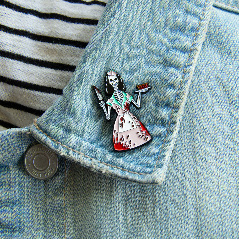 A pin of a bloody skeleton waitress brandishing a knife. Worn on the lapel of a denim jacket for goth and gothabilly style. 