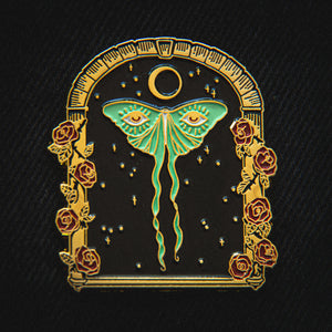 A witchy enamel pin of a luna moth in an archway of flowers for women's magical fashion.