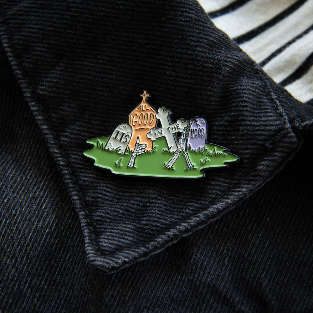 A death positive enamel pin for men and women on the lapel of a black denim jacket.