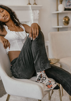 A stylish woman wearing red, beige, and black socks printed with moths, snakes, skulls, and hearts. 