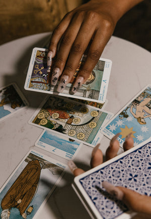 A woman reading tarot cards with a witchy manicure of nail stickers featuring mushrooms, moths, stars, and flowers. 