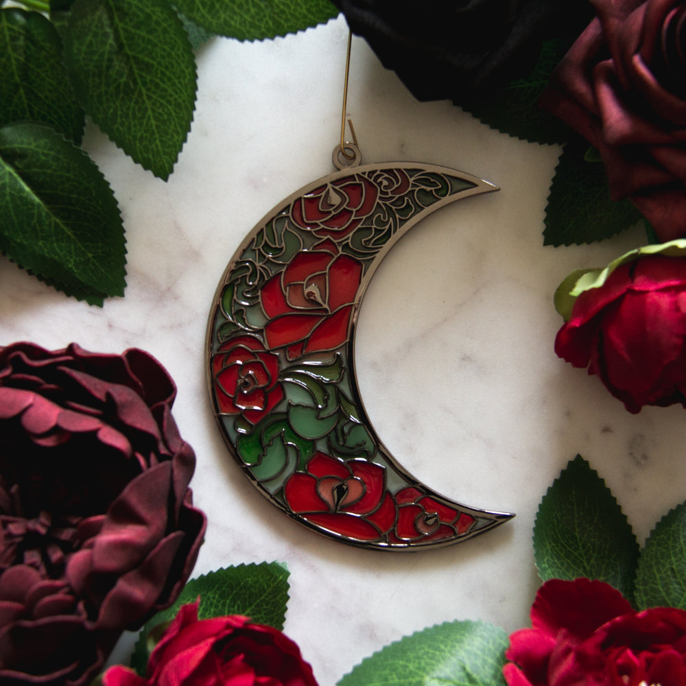 Witchy christmas ornament of a moon with red and green roses inside. 