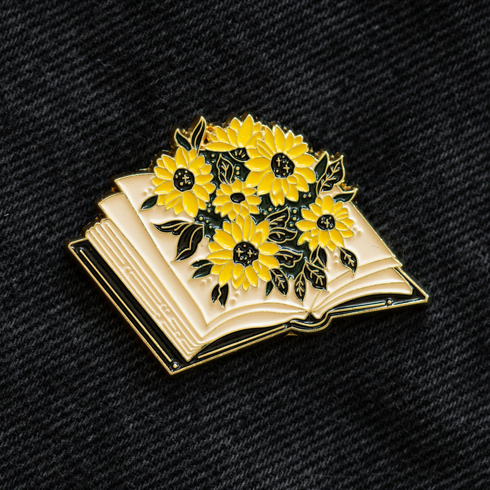 A dark academia fashion lapel pin brooch of a library book with flowers. 