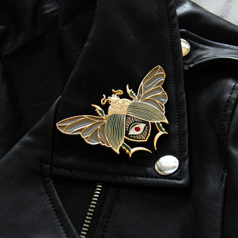 A cool black, gold, and green brooch of a large scarab beetle on the lapel of a leather jacket for elevated luxury punk fashion.