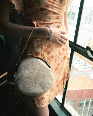 A cute vintage style clasp purse in white leather with gold hardware that converts from a crossbody to a top handle. 