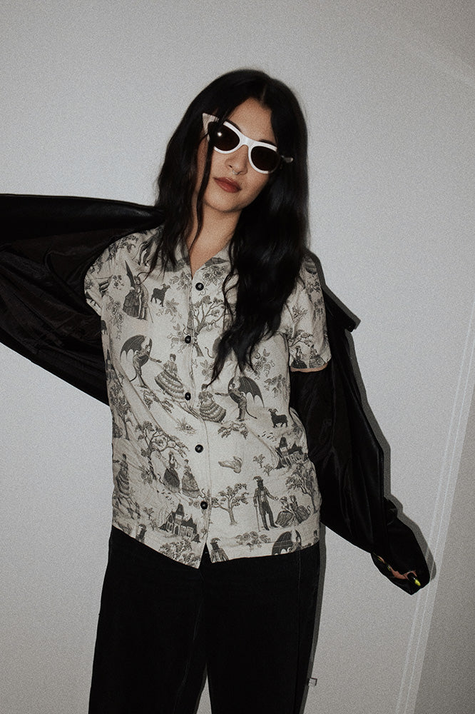 Women's short sleeve button down shirt with toile print of a victorian haunted mansion, black philip, devils, and demons.