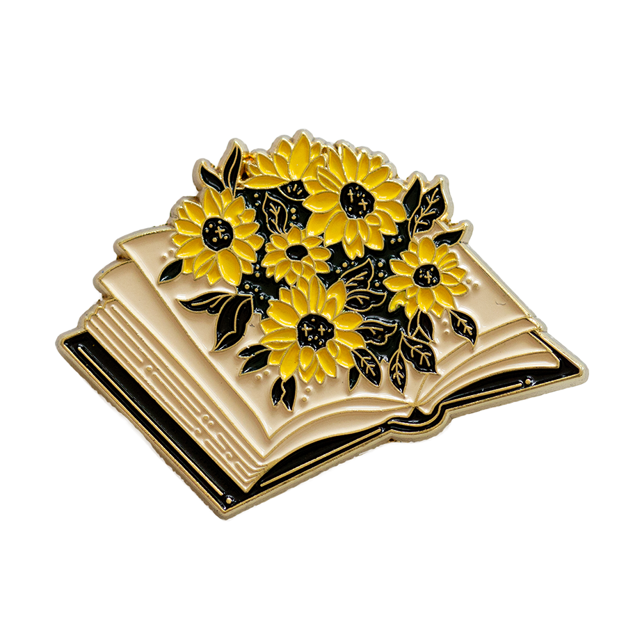 A cute enamel pin of an open book blooming with sunflowers. 