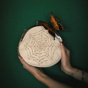 A butterfly landed on a spiderweb purse for cottagecore and alternative aesthetic fashion. 