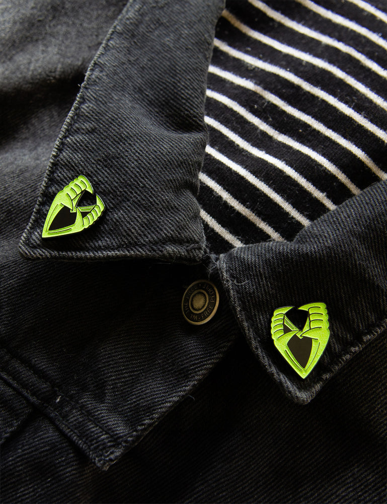 Glow-in-the-dark vampire teeth enamel pins on the collar points of a jacket. 