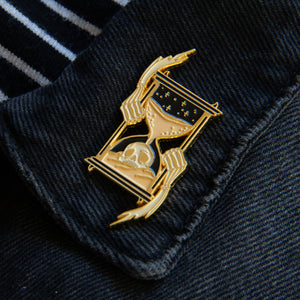 A death positive enamel pin for men and women featuring a skull in an hourglass. 