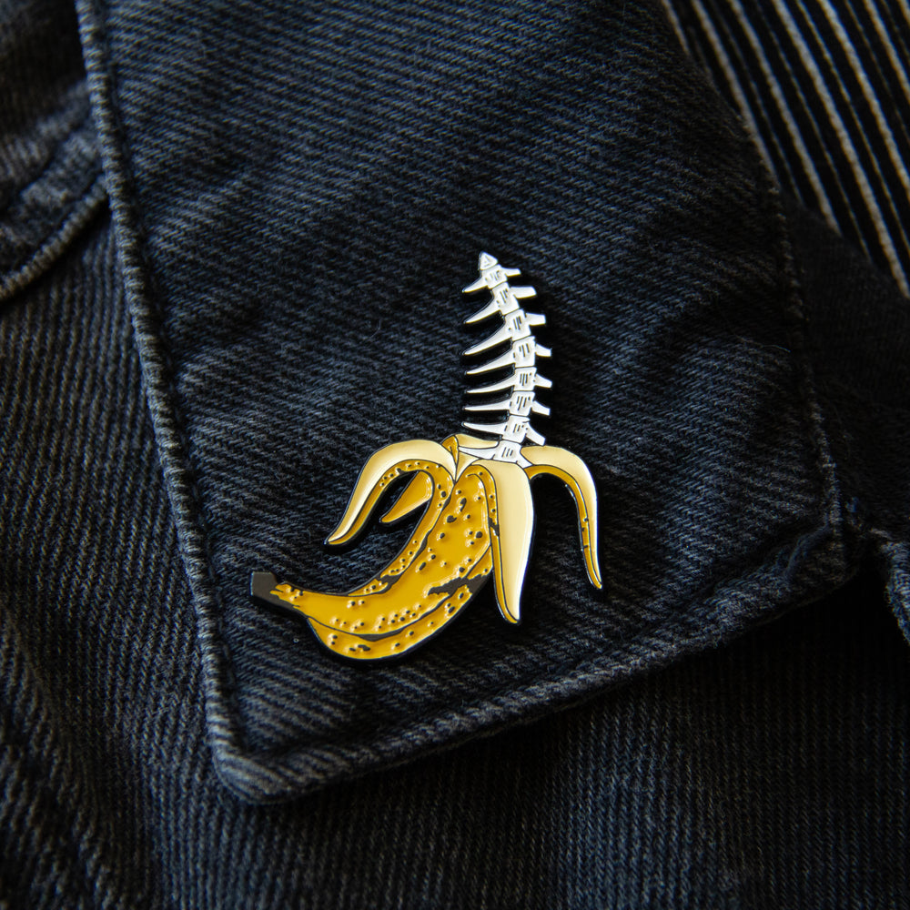 A quirky tropical enamel pin worn on the lapel of a black denim jacket.