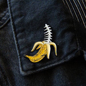 A quirky tropical enamel pin worn on the lapel of a black denim jacket.