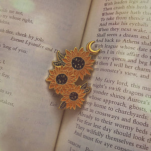 A sunflower enamel pin pictured in a copy of "A Midsummer Night's Dream" for victorian and dark academia inspired women's fashion.