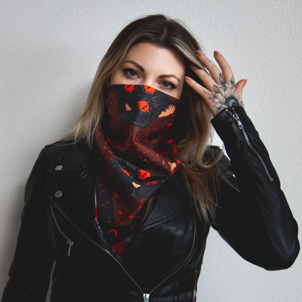 A tattooed woman wearing a red bandana printed with black cats for alternative and goth style. 