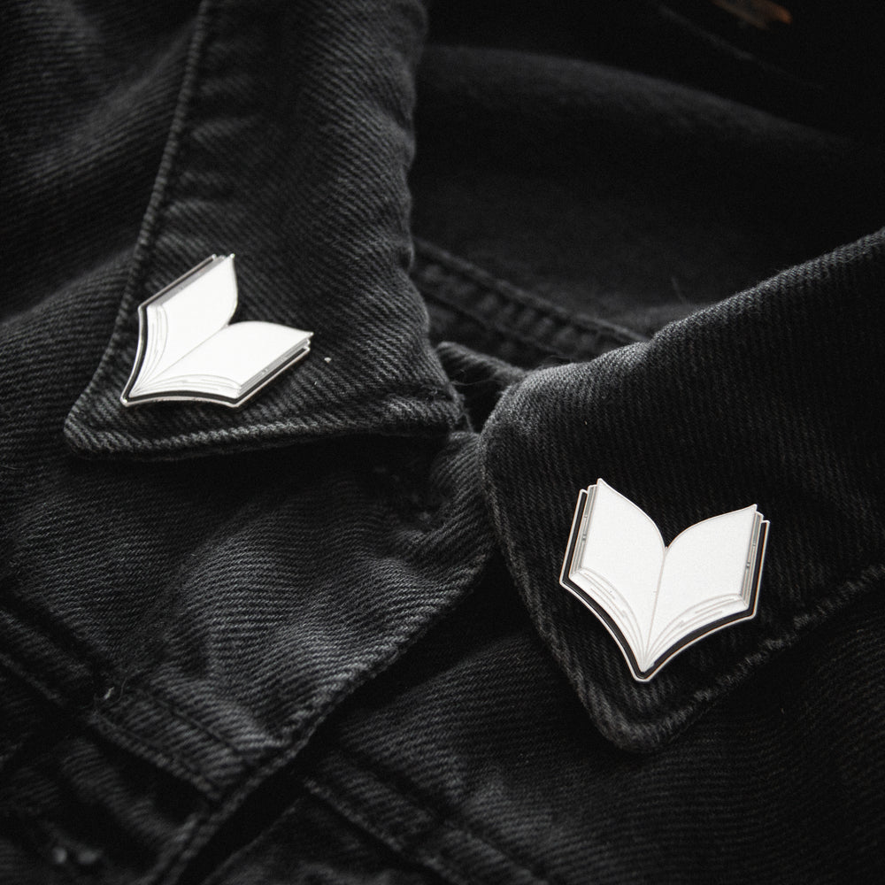 A set of enamel collar pins shaped like open books in black, silver, and white. 