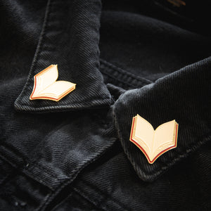 
            
                Load image into Gallery viewer, Two enamel pins of open books in red and gold. These pins can be worn on the collar of a shirt or jacket. 
            
        