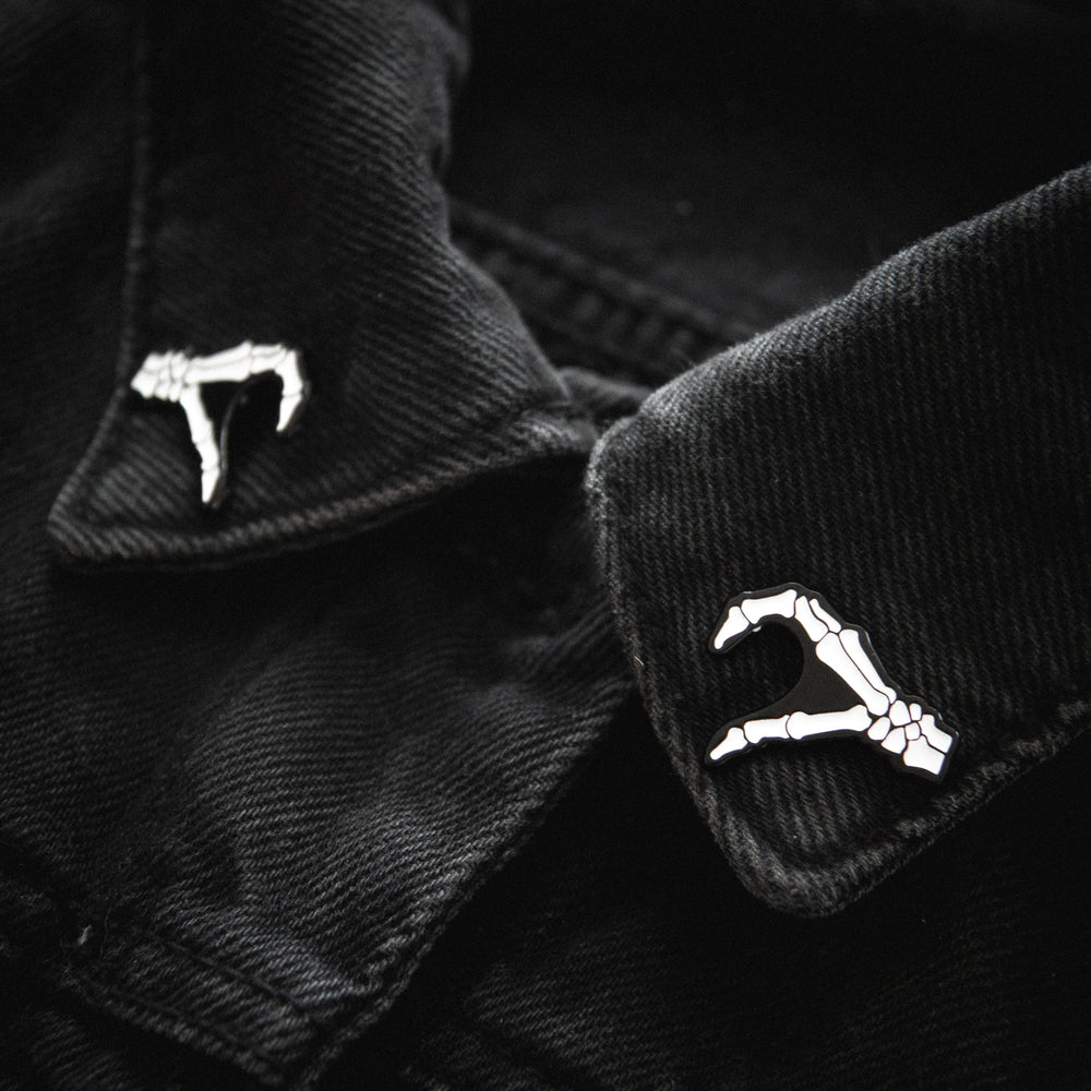 Two black and white skeleton hand pins worn on the collar of a dress shirt for cool alternative fashion. 