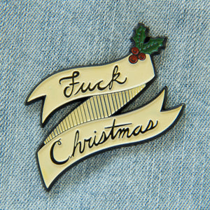 A funny enamel pin of a banner with holly and the quote, "Fuck Christmas".