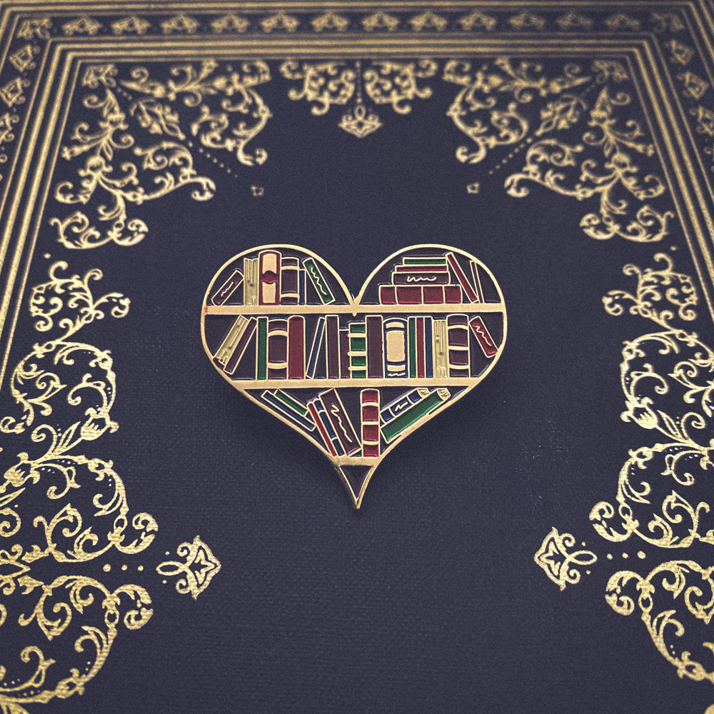 An enamel pin of a heart shaped bookshelf pictured on an antique book for dark academia fashion.