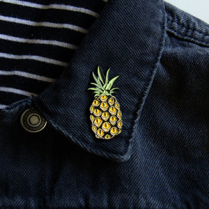 A tropical enamel pin of pineapple fruit on the lapel of a men's denim jacket. 