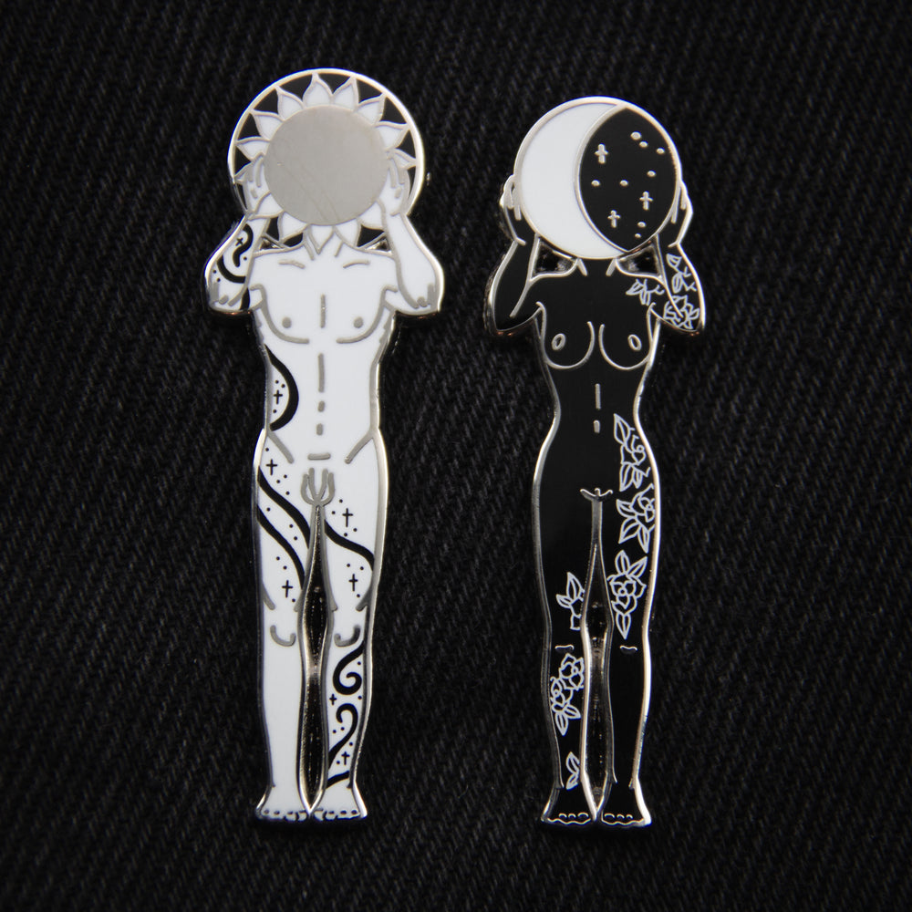 A beautiful enamel pin set in silver, black, and white of a tattooed man holding a sun and a woman holding a moon for couple's gifts.