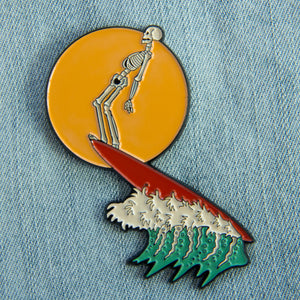 Enamel pin of a skeleton surfing on a wave. Designed by artist Ectogasm. 