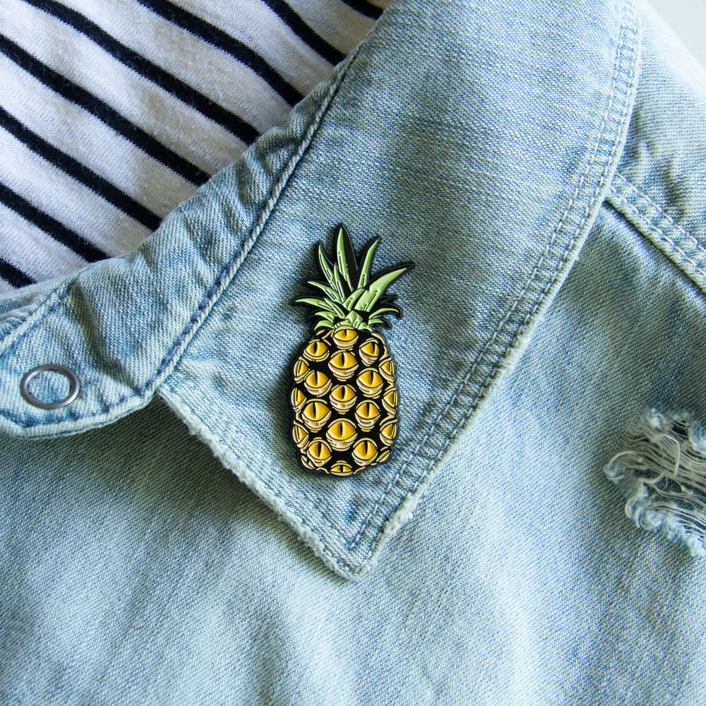 A cool enamel pin of a pineapple with spooky eyes. Made with black metal and yellow enamel. 