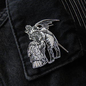 A witchy collectible gift of a victorian dressed woman kissing a Devil, worn on a black denim jacket lapel.